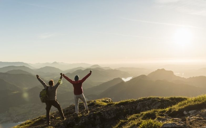 Bilde av to mennesker på en fjelltopp med hendene i været